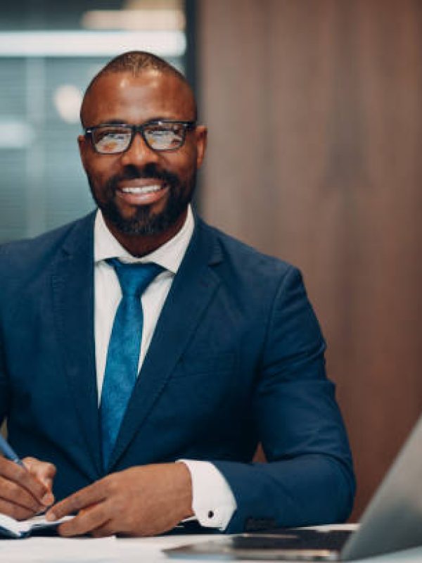 Portrait smiling african american businessman in blue suit sit at table for meeting in office with notebook with pen and laptop